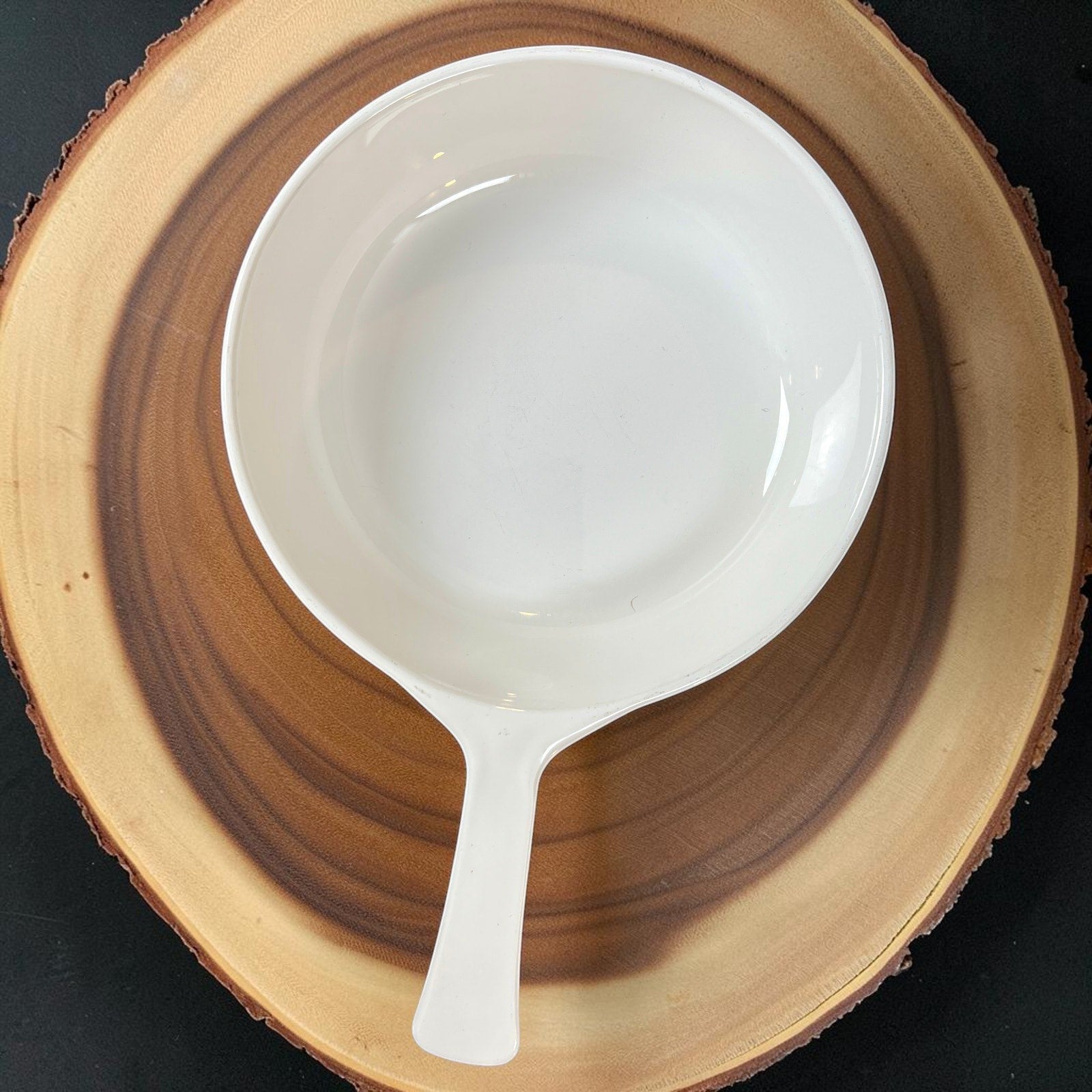 A vintage white Corning Ware P-83-B skillet pan with an integrated handle, resting on a round wooden cutting board. - Photo 2