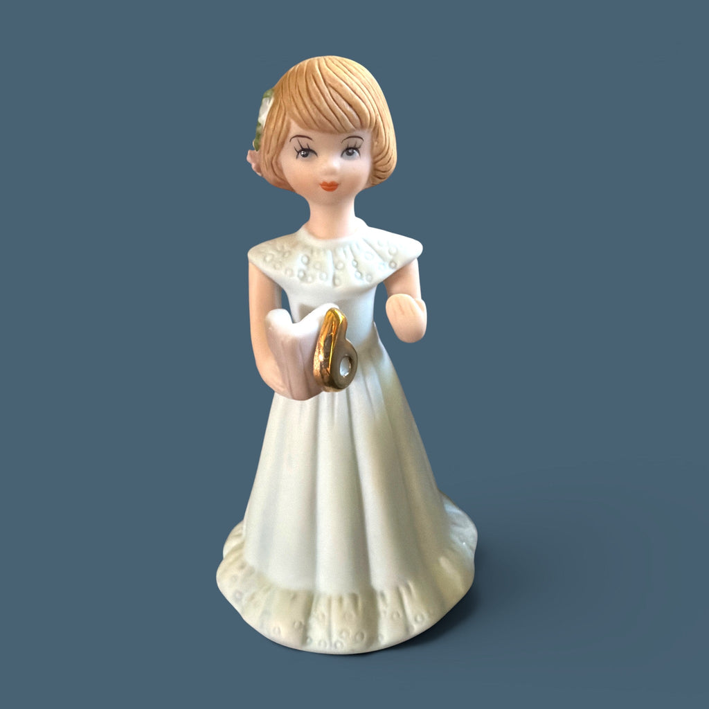 Vintage Enesco Growing Up Girls Age 6 porcelain figurine showing a fair child wearing a delicate white floor-length dress decorated with a classic high collar, a soft ruffled hemline, and a prominent bow tied at the back. - Photo 1