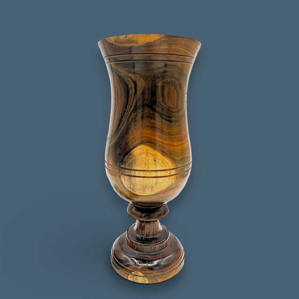 A vintage hand-turned wood chalice vase with a flared rim and a stout pedestal base, displaying a highly figured grain with rich brown and golden hues and fine concentric incised lines around the body against a solid dark grey background. - Photo 1
