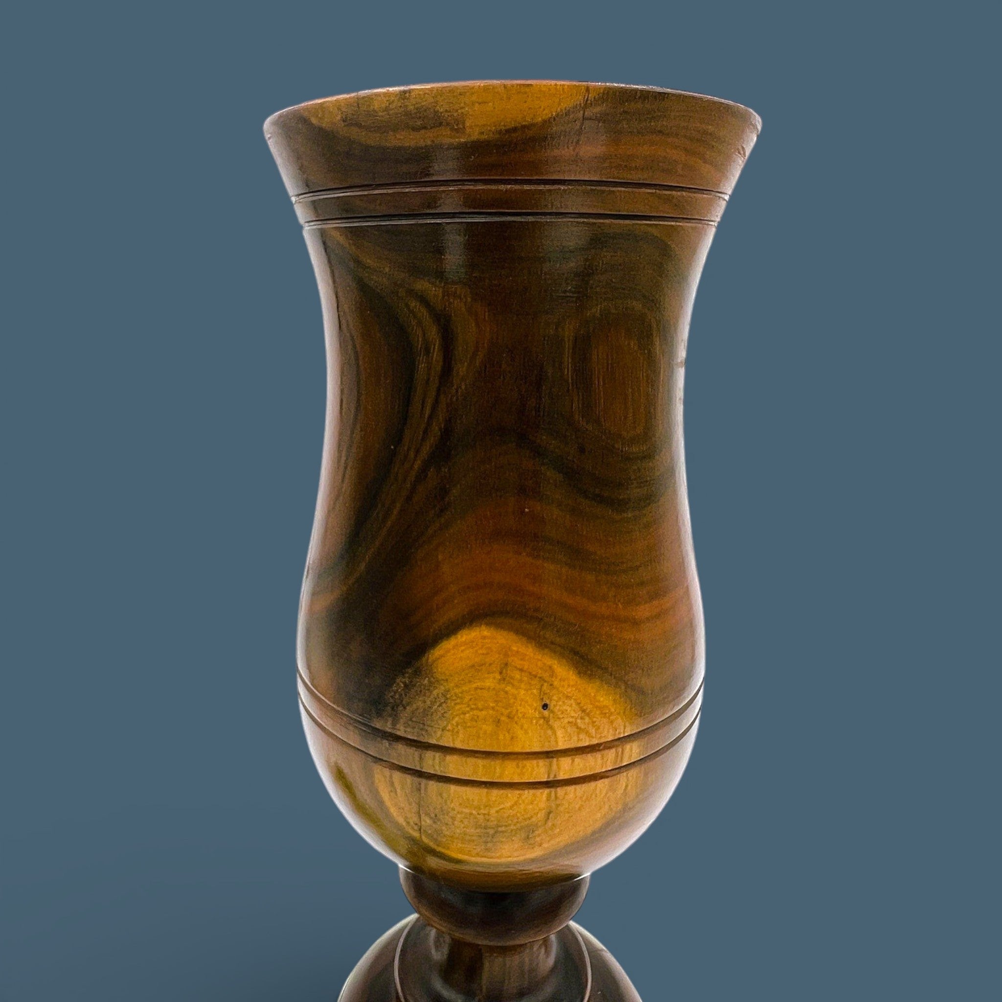 A vintage hand-turned wood chalice vase with a flared rim and a stout pedestal base, displaying a highly figured grain with rich brown and golden hues and fine concentric incised lines around the body against a solid dark grey background. - Photo 5