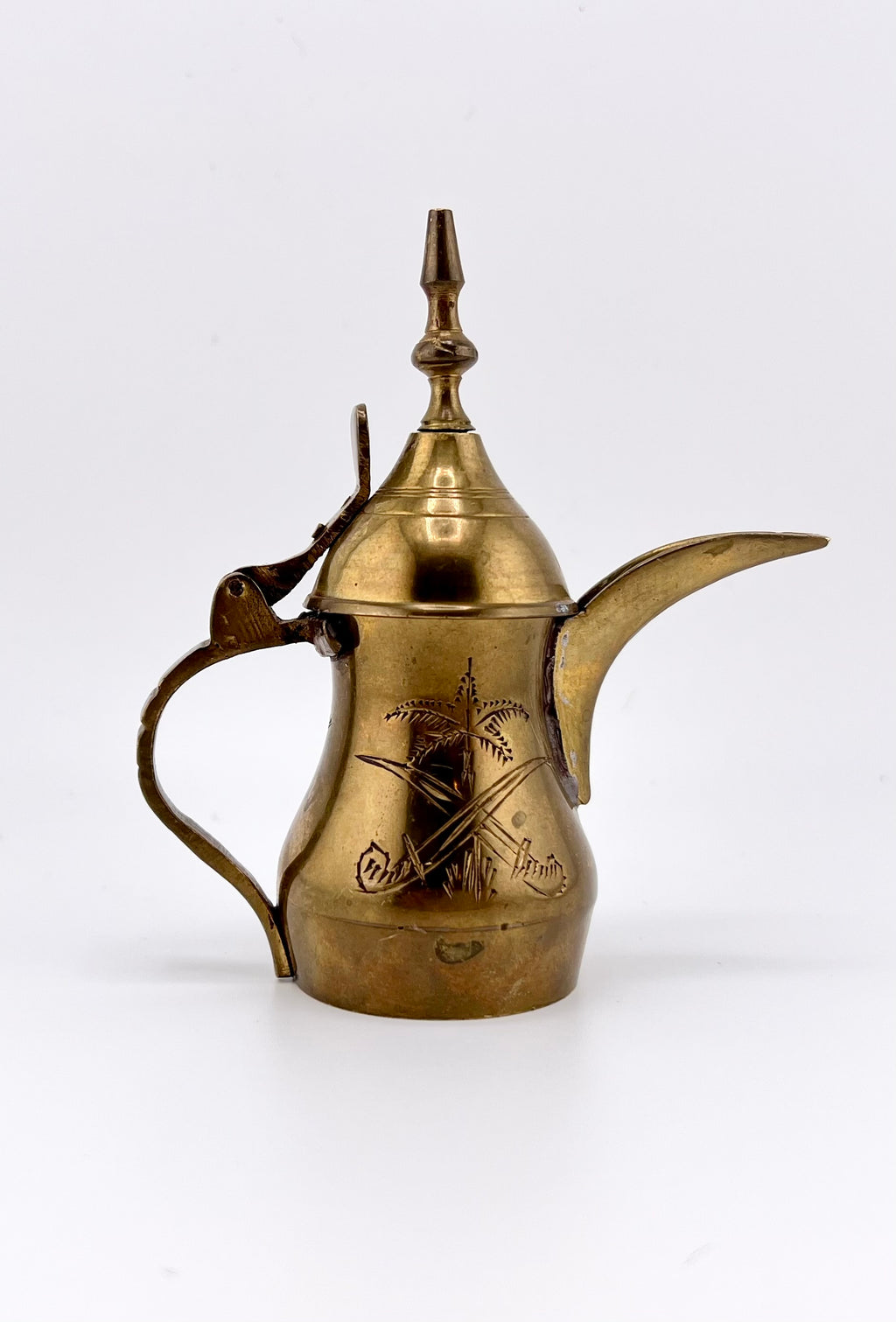 A miniature vintage brass dallah coffee pot featuring hand-chased floral engravings, an elongated curved spout, a rounded body, a side handle, and a hinged conical lid. - Photo 1