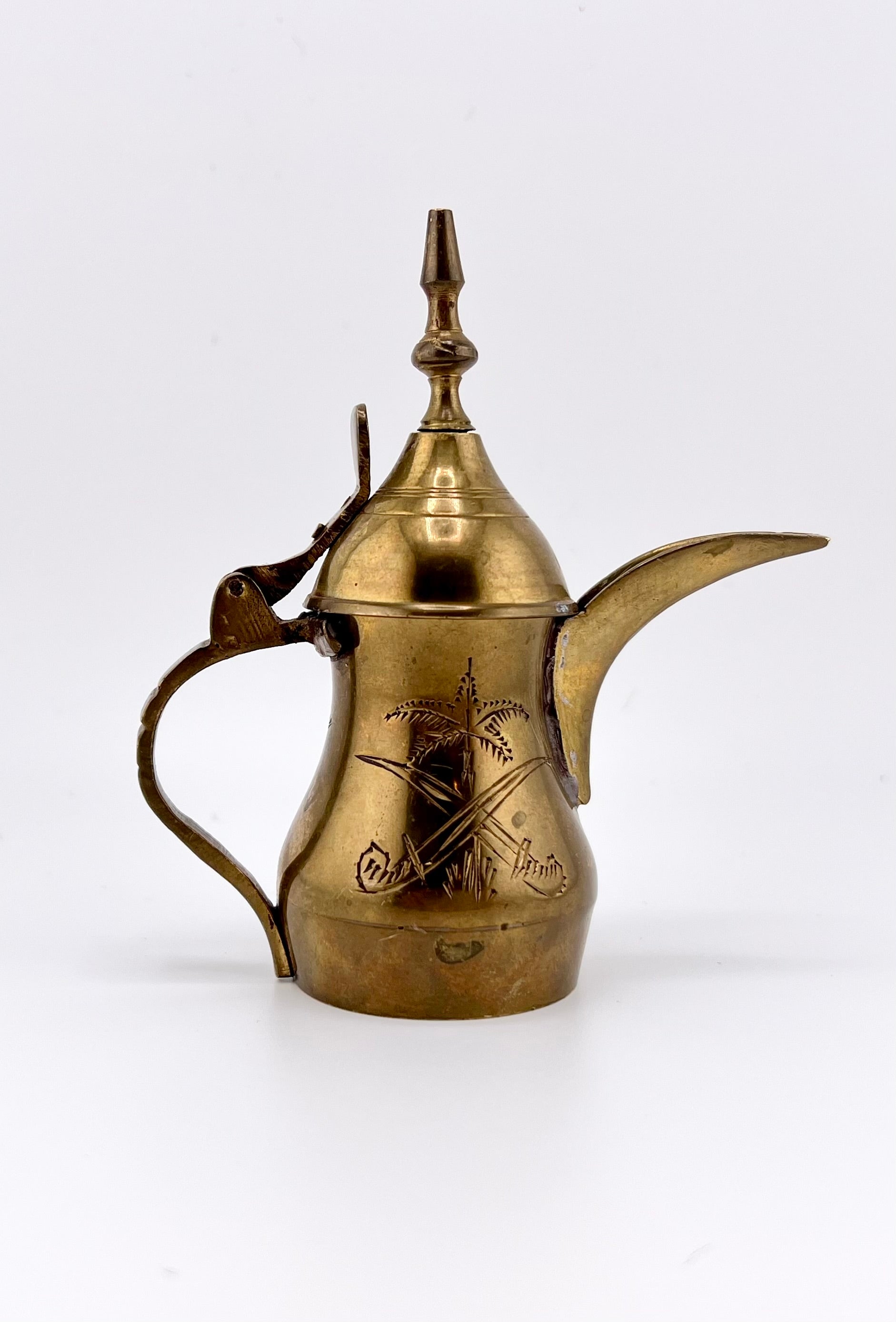 A miniature vintage brass dallah coffee pot featuring hand-chased floral engravings, an elongated curved spout, a rounded body, a side handle, and a hinged conical lid. - Photo 1