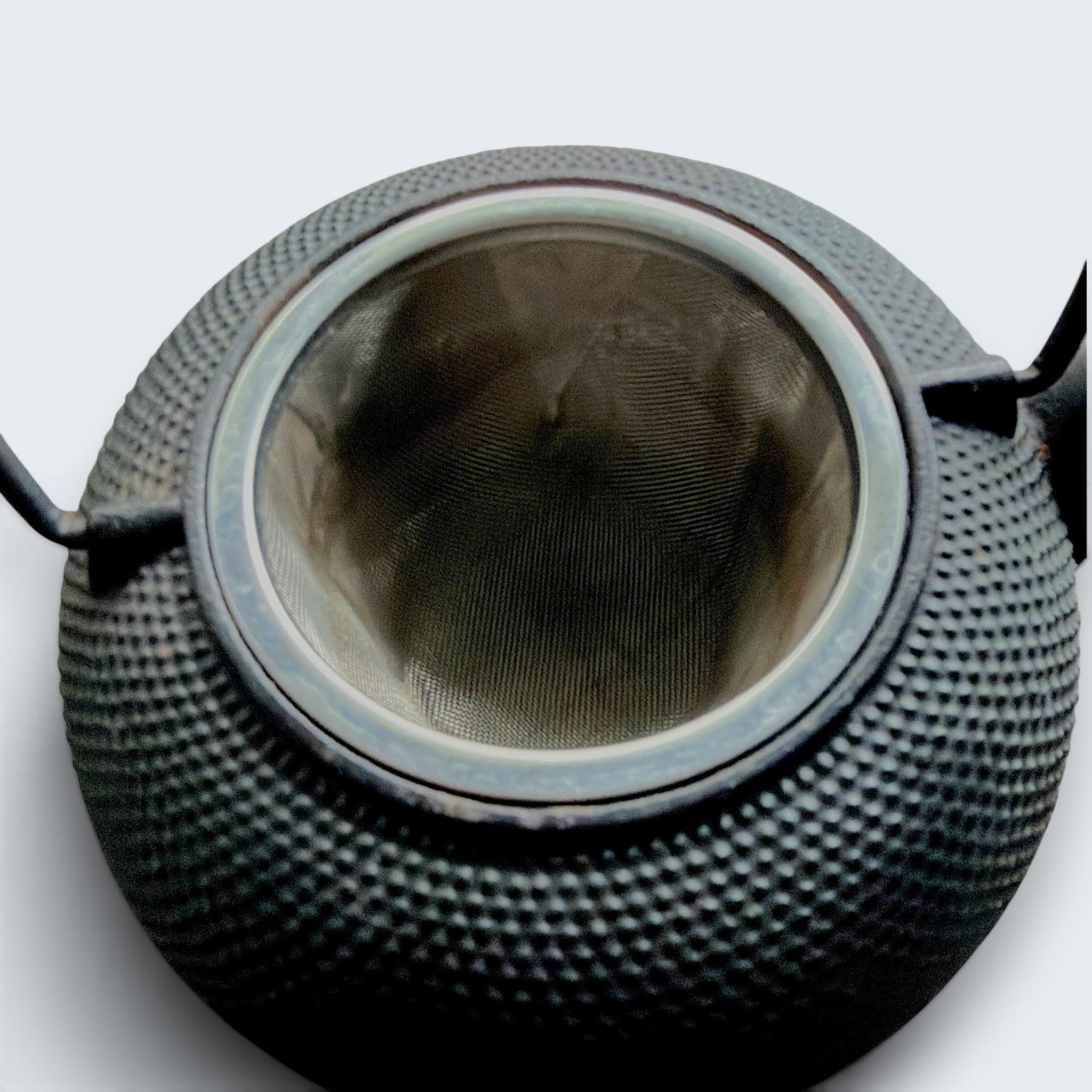 A black cast iron tetsubin teapot featuring a classic hobnail textured surface, open top showing a stainless steel mesh infuser basket, and two pivoting black metal handle hinges on the sides. - Photo 10