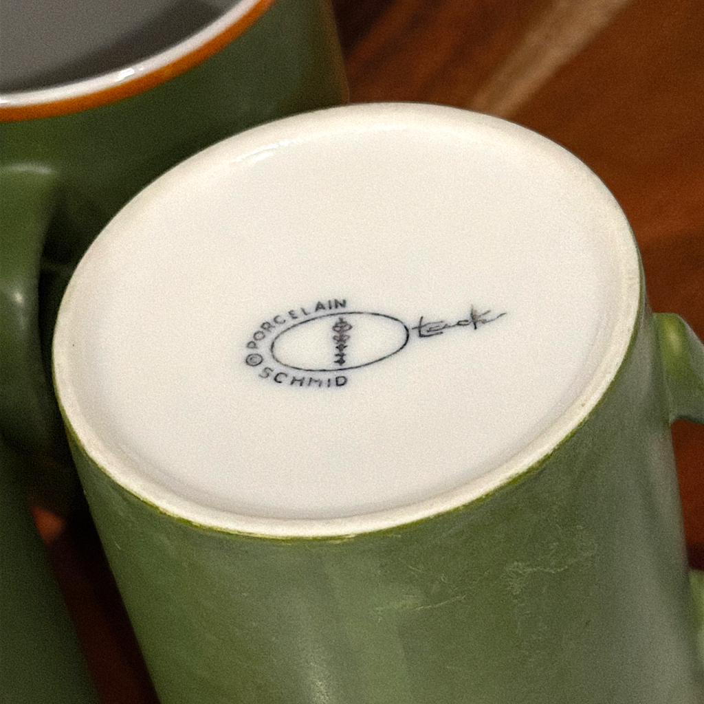 A mid-century modern cylindrical green porcelain mug featuring a bold orange stripe along the upper rim, a white interior, and an attached side handle, standing upright on a round wooden surface. - Photo 2