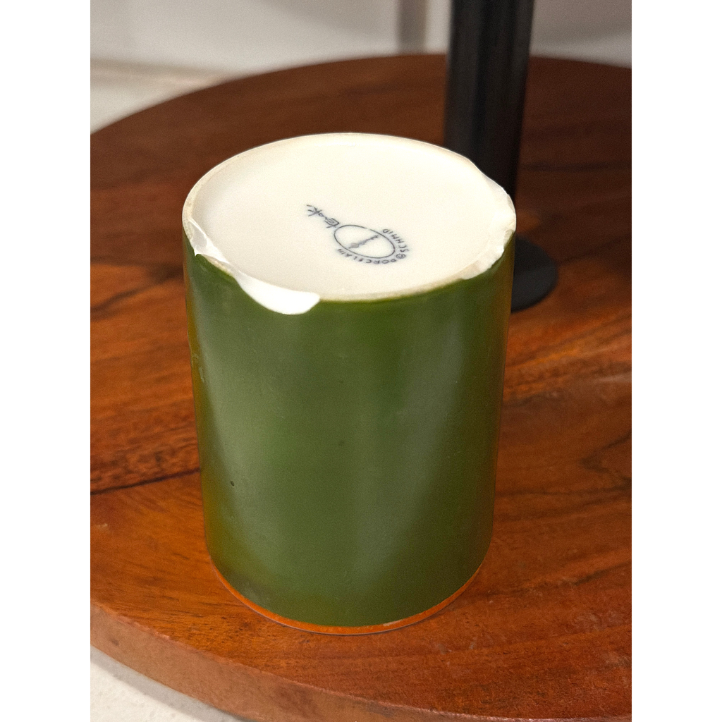A mid-century modern cylindrical green porcelain mug featuring a bold orange stripe along the upper rim, a white interior, and an attached side handle, standing upright on a round wooden surface. - Photo 3