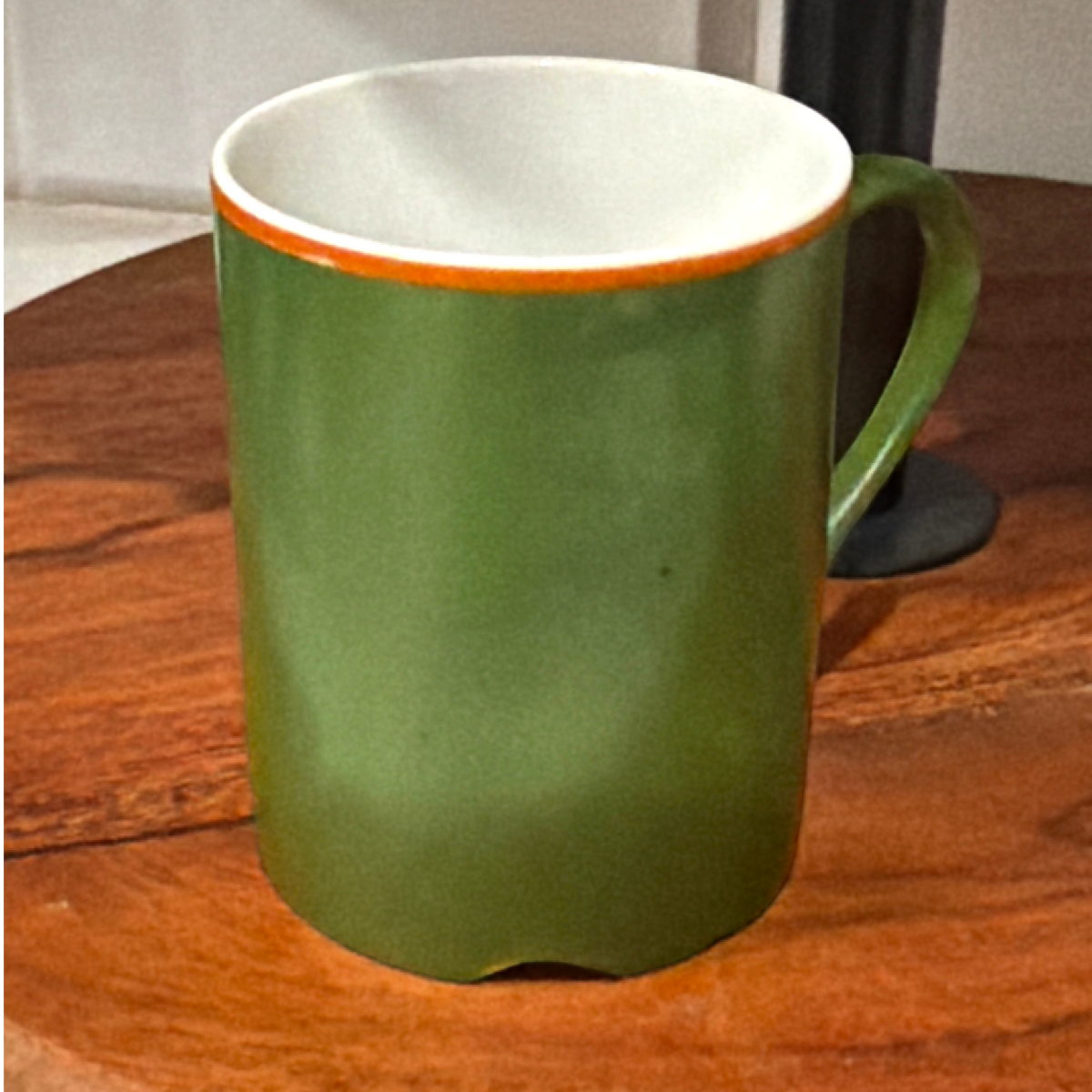 A mid-century modern cylindrical green porcelain mug featuring a bold orange stripe along the upper rim, a white interior, and an attached side handle, standing upright on a round wooden surface. - Photo 4