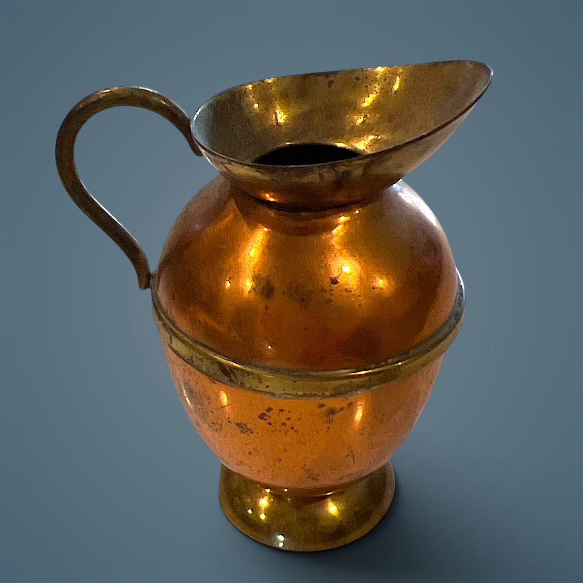Vintage Peerage copper miniature pitcher with a flared brass rim, rounded body, applied brass waist band, and brass loop handle resting on a pedestal base. - Photo 1