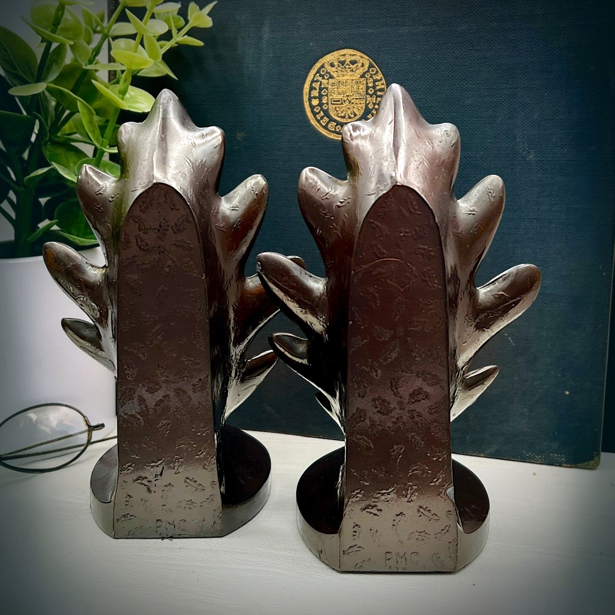 A pair of vintage PMC hand-cast metal oak leaf bookends with a rich bronze finish, designed with stylized lobed leaves and delicate embossed cascading leaf patterns on their curved backs, supporting a dark book on a white surface. - Photo 4