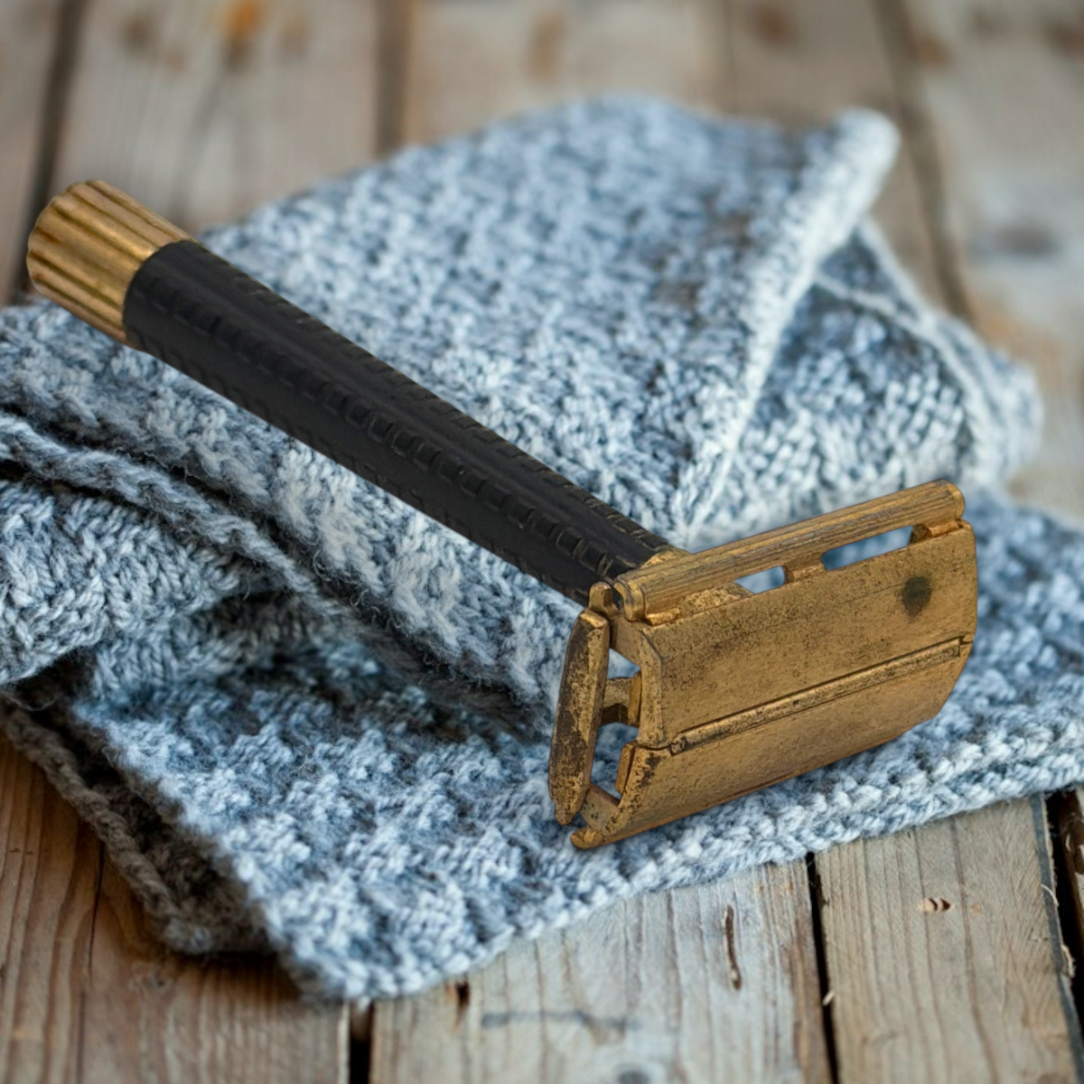 Vintage gold-tone Schick Krona double-edge safety razor resting closed on a textured grey knitted cloth against a rustic wooden surface, showing its brass butterfly head and ribbed black handle. - Photo 1