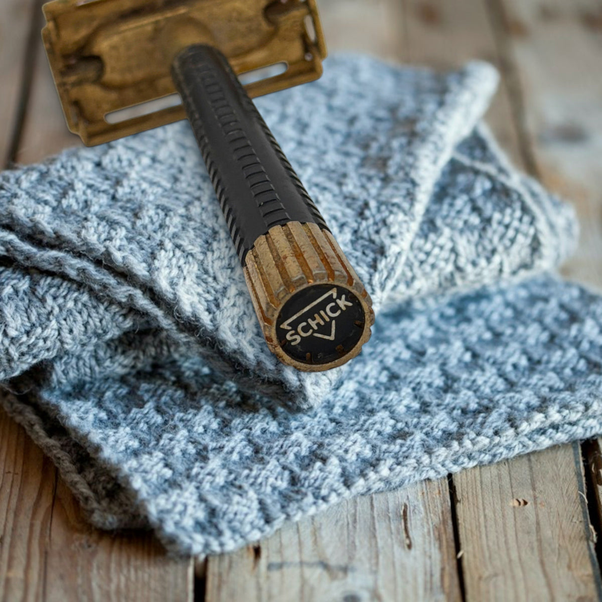 Vintage gold-tone Schick Krona double-edge safety razor resting closed on a textured grey knitted cloth against a rustic wooden surface, showing its brass butterfly head and ribbed black handle. - Photo 2