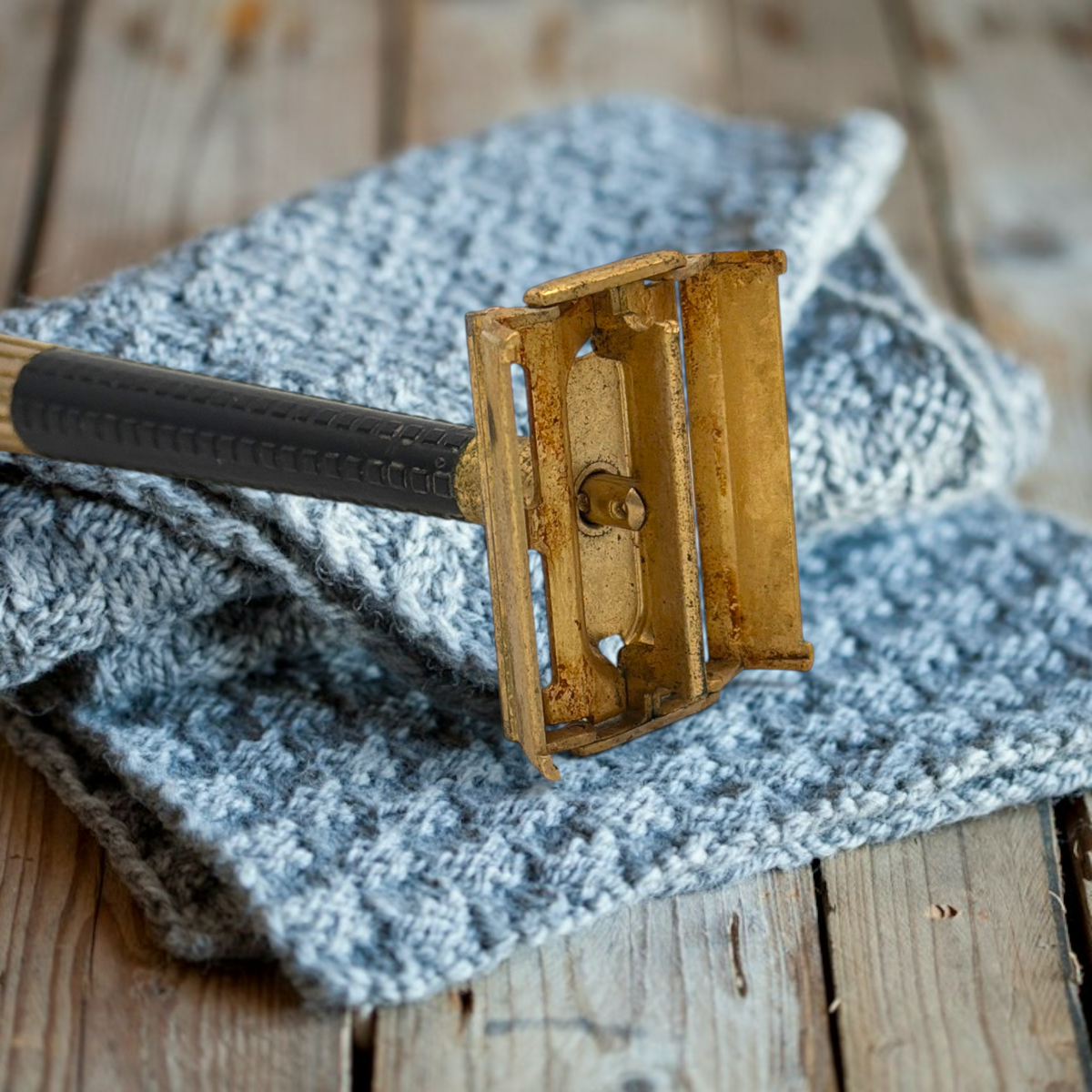 Vintage gold-tone Schick Krona double-edge safety razor resting closed on a textured grey knitted cloth against a rustic wooden surface, showing its brass butterfly head and ribbed black handle. - Photo 4