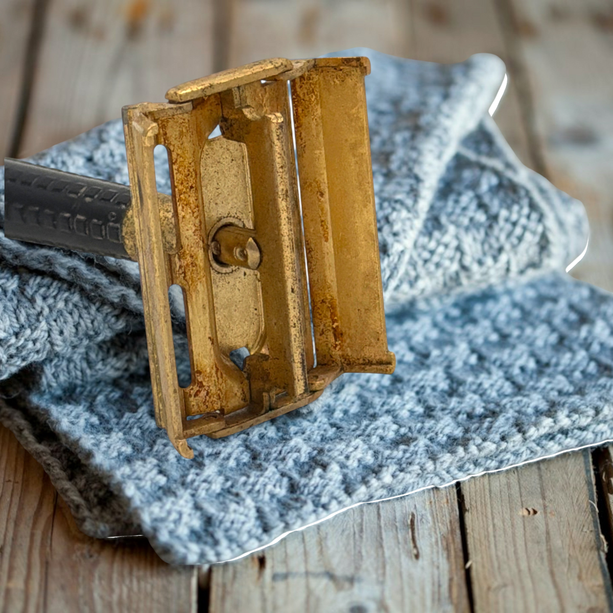 Vintage gold-tone Schick Krona double-edge safety razor resting closed on a textured grey knitted cloth against a rustic wooden surface, showing its brass butterfly head and ribbed black handle. - Photo 5