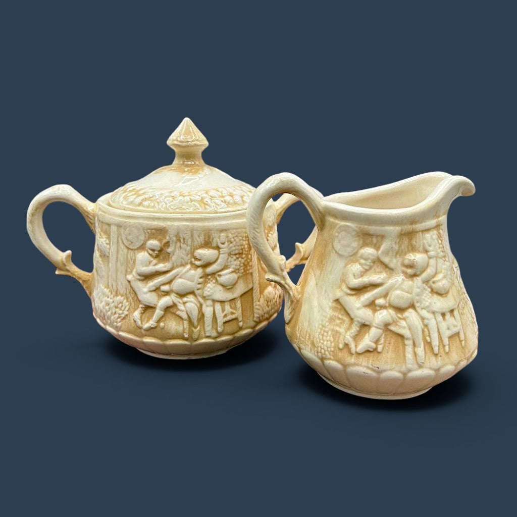 A cream-colored antique ceramic creamer pitcher featuring detailed relief-molded scenes of tavern figures under a smooth glazed finish. - Photo 2