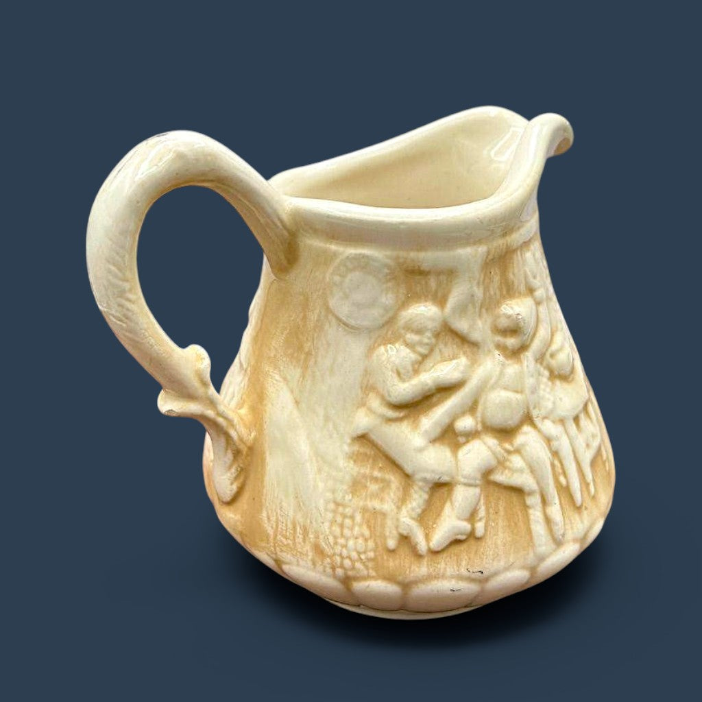 A cream-colored antique ceramic creamer pitcher featuring detailed relief-molded scenes of tavern figures under a smooth glazed finish. - Photo 7