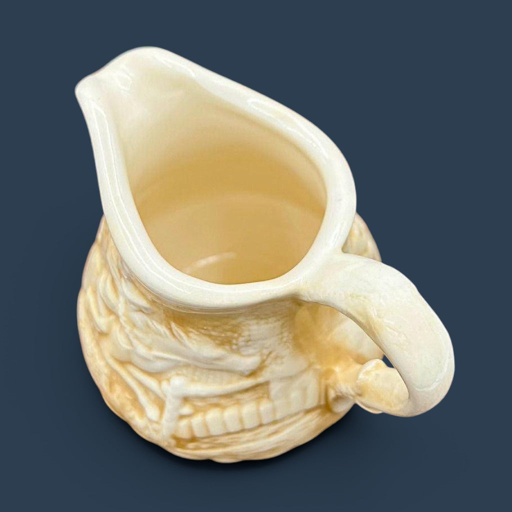 A cream-colored antique ceramic creamer pitcher featuring detailed relief-molded scenes of tavern figures under a smooth glazed finish. - Photo 8