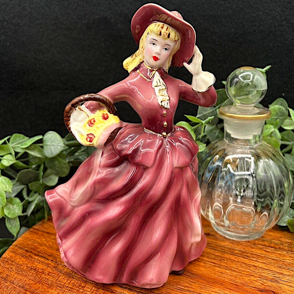 Vintage Ucagco ceramic figurine of an elegant Victorian lady wearing a glossy mauve dress, wide-brimmed bonnet, and white gloves while carrying a flower basket. - Photo 1